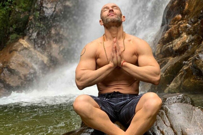 A muscular man in a meditative pose with a waterfall in the background. 3
