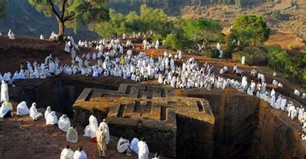 A large group of people gathered around an ancient stone structure in a natural setting. 3