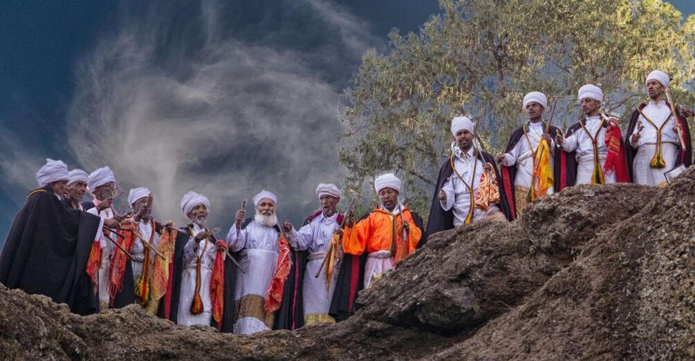 A group of men in traditional attire standing on a rocky outcrop with a cloudy sky in the background. 5