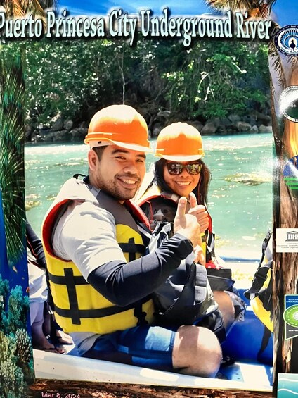 Two people in a boat wearing life jackets and helmets, with a river and greenery in the background. 5