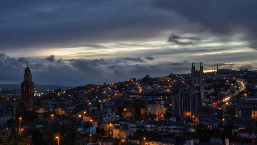 A cityscape at dusk with illuminated streetlights, a prominent church, and a clock tower. 1