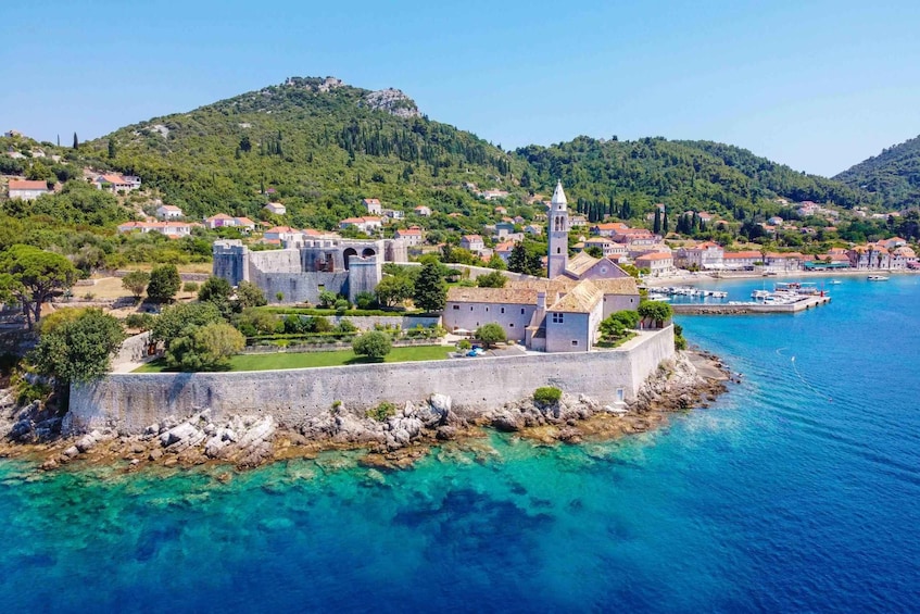 A coastal town with a historic fortification, clear turquoise waters, and lush green hills in the background. 1