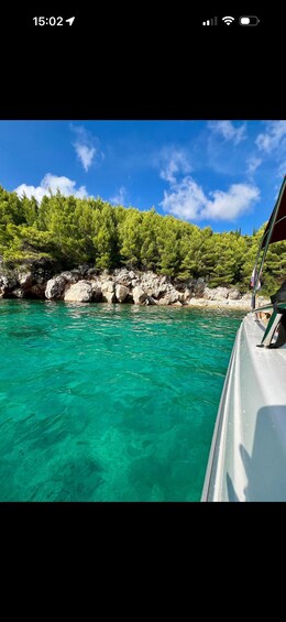 A boat on turquoise water with a rocky shoreline and dense green trees under a clear blue sky. 3