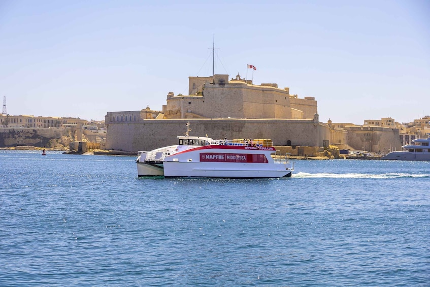 A boat named MAPFRE MIDDLESSEA on a body of water with a large fort-like structure in the background. 1
