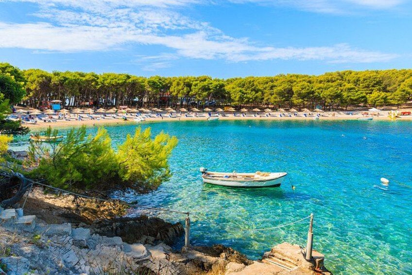 Un mare azzurro e trasparente, una barca, una costa rocciosa e una spiaggia con alberi. 2
