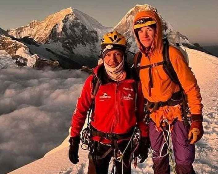 Two climbers on a snowy mountain peak with a clear sky and clouds below. 5