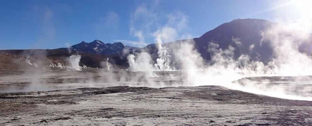 A geothermal area with steam vents and a mountainous backdrop. 3