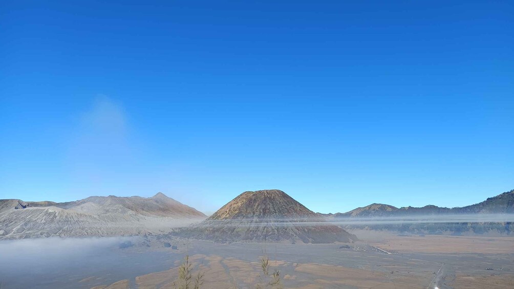 A volcanic landscape with a prominent mountain in the center, surrounded by barren terrain and a clear blue sky. 5