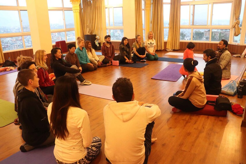 A group of people sitting on yoga mats in a room with large windows. 3