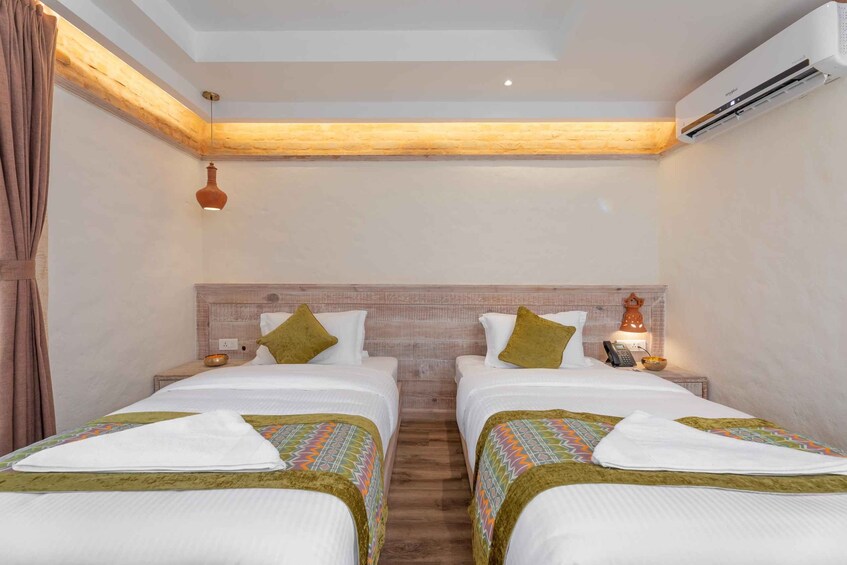 A hotel room with two beds, wooden beams, a hanging light, and an air conditioning unit. 2