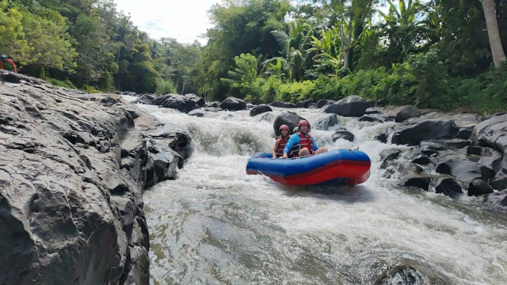 A person in a blue inflatable raft navigating a river with rapids, surrounded by rocky terrain and dense greenery. 4