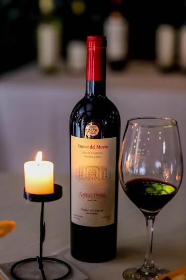 A bottle of Tannat del Museo wine and a glass of red wine on a table with a lit candle. 2