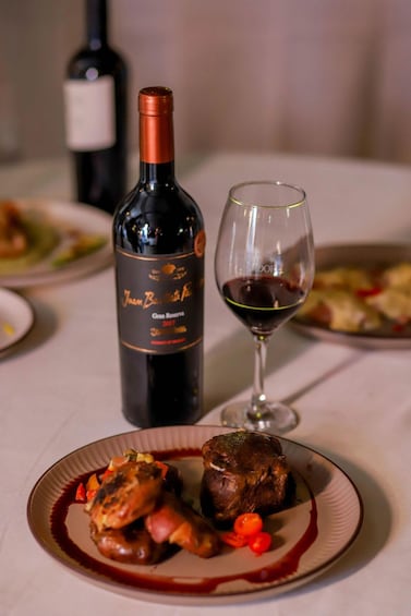 A bottle of wine, a glass with red wine, and a plate with food. 5