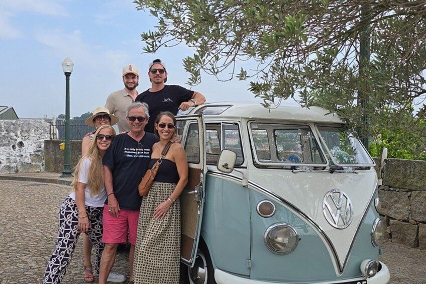 Un vieux camping-car Volkswagen est garé sur une rue pavée, et un groupe de personnes pose devant. 2