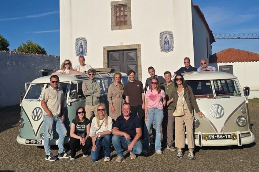 Un gruppo di persone che posa di fronte a un edificio bianco con un furgone Volkswagen. 3