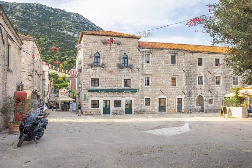 A stone building with a green awning, a parked motorcycle, and a mountain in the background. 2