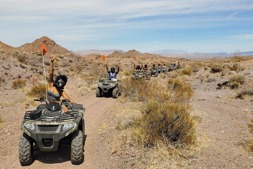 Off-road vehicles on a dirt path in a desert landscape with sparse vegetation and distant mountains. 3