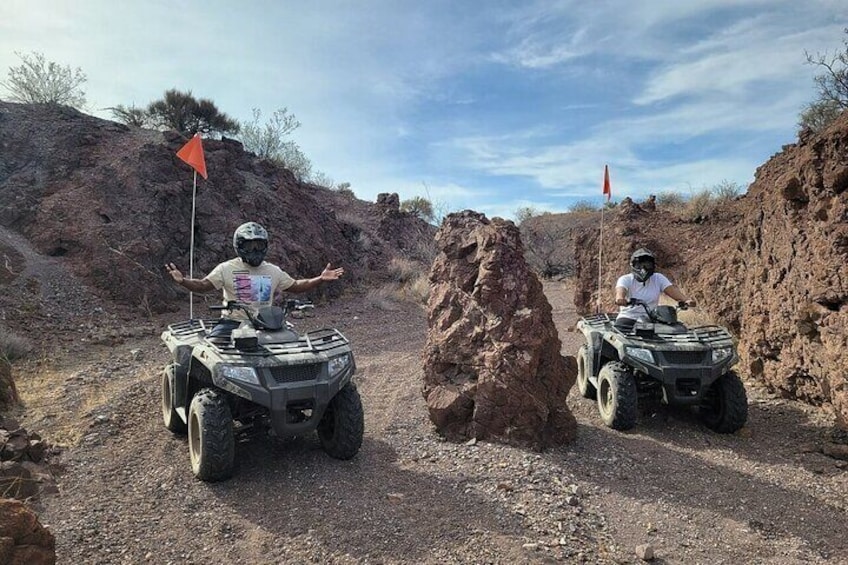 Two people on ATVs on a rocky dirt path with red flags. 4