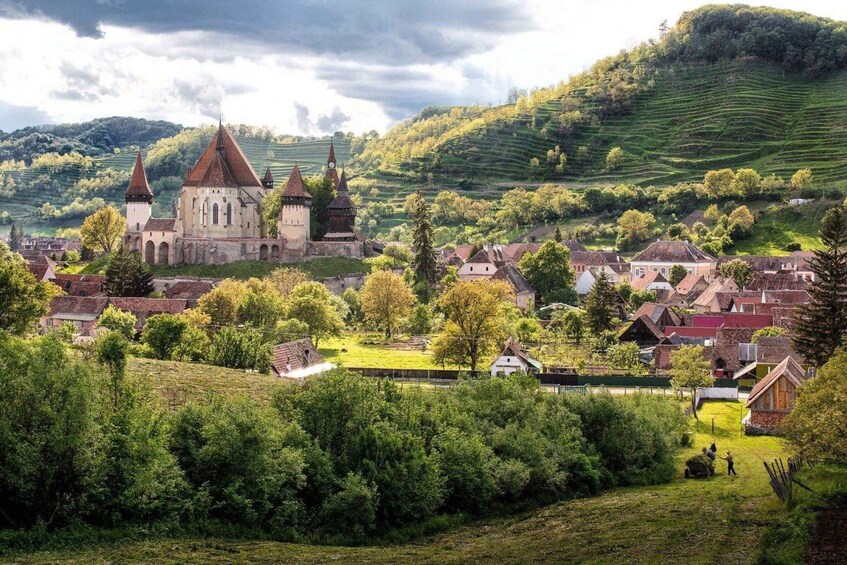 A historic town with a prominent church featuring multiple spires, surrounded by lush green hills and scattered houses. 5