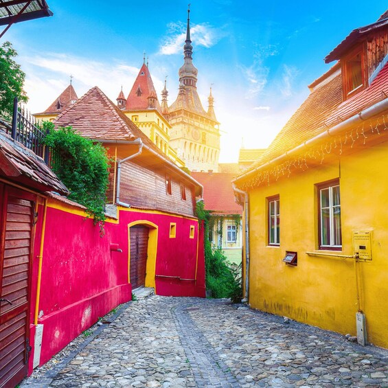 A cobblestone street flanked by colorful buildings, a church with a tall spire, and a clear blue sky. 1