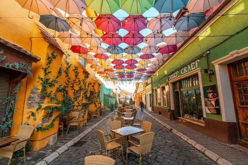 A cobblestone street with colorful umbrellas hanging overhead, creating a vibrant canopy. 3