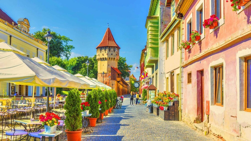 A cobblestone street lined with colorful buildings, outdoor cafes, and a historic tower. 2