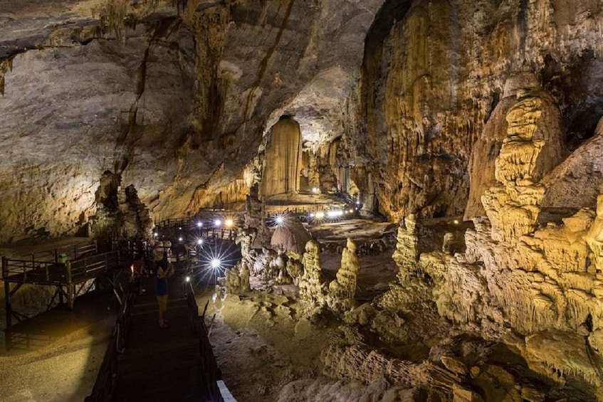 A cave with stalactites and a central chamber illuminated by lights. 1