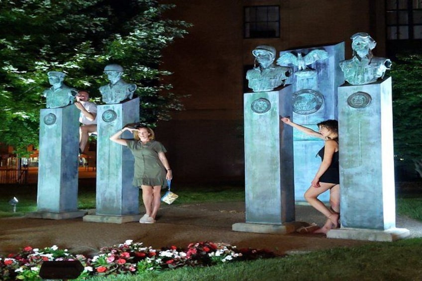 A sculpture of two figures on pedestals with a woman posing in front. 3