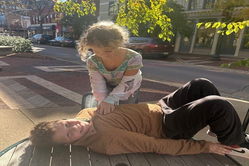 A person lying on a bench outdoors with another person standing beside them. 4