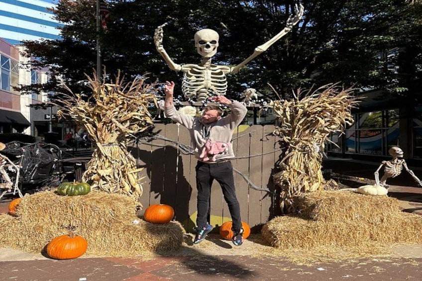 A person in a skeleton costume standing in front of a scarecrow and a skeleton figure. 5
