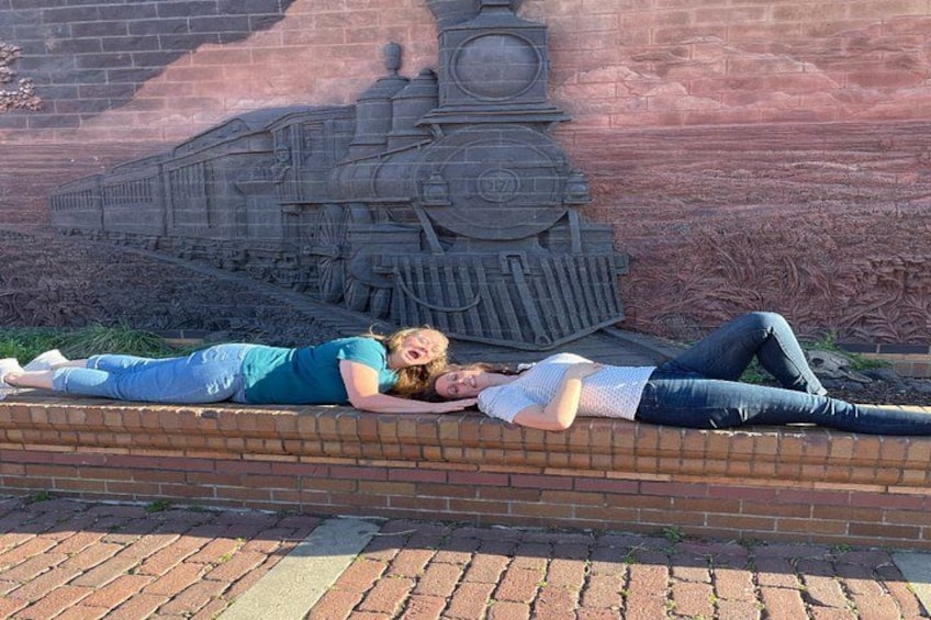 Two people lying on a brick wall with a mural of a train in the background. 3