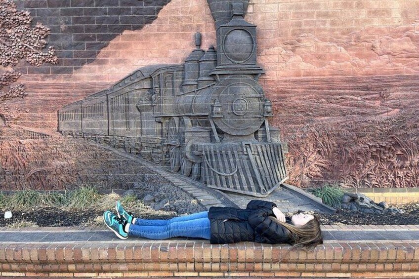 A person lying on a sidewalk with a mural of a train in the background. 2