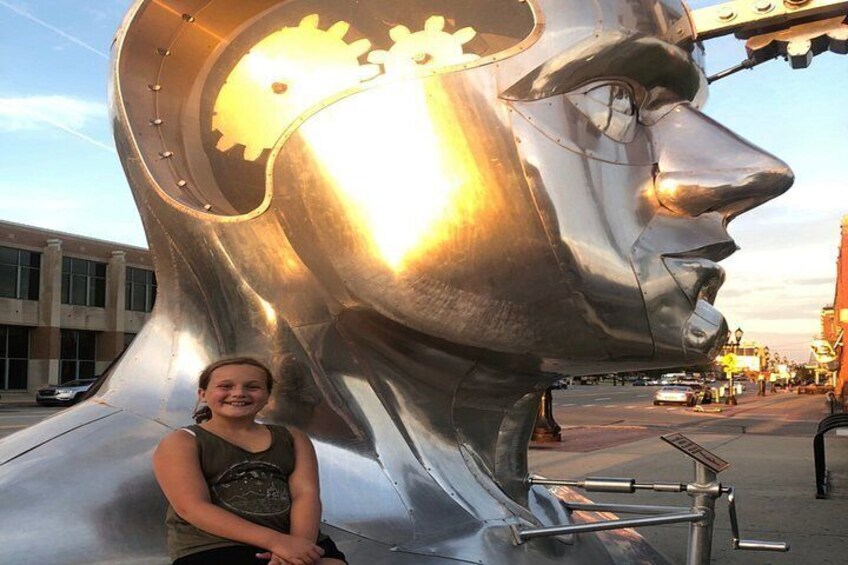 A person standing in front of a large metallic sculpture with gears and a face. 5