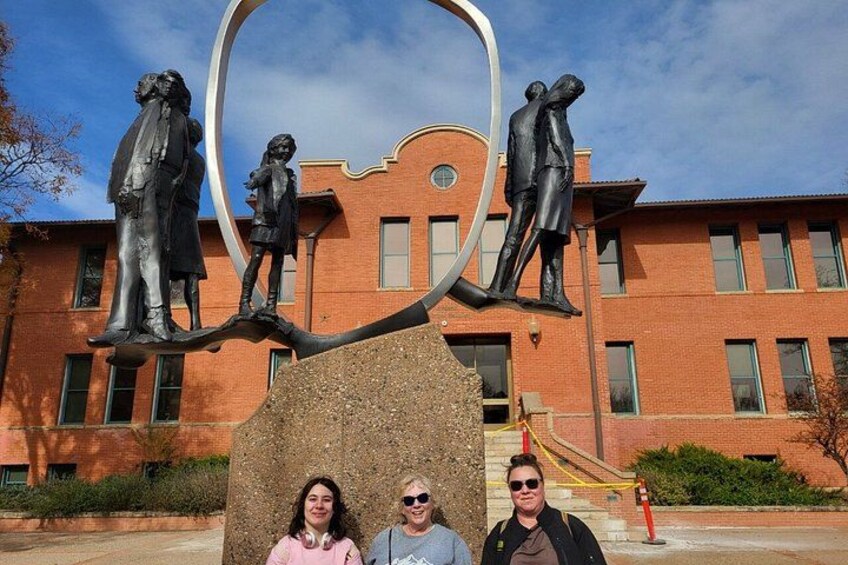 A sculpture of people on a rock with a building in the background. 1