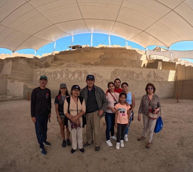 A group of people standing in front of ancient ruins under a large tent. 2