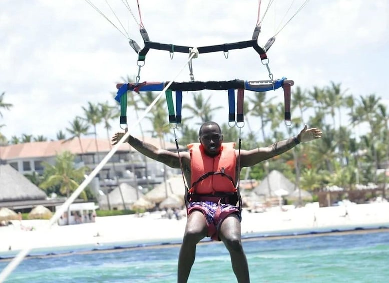 A person parasailing over water with a beach and palm trees in the background. 2