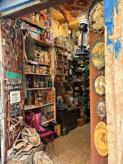 A cluttered shop with shelves full of various items, including bottles, boxes, and decorative plates. 4