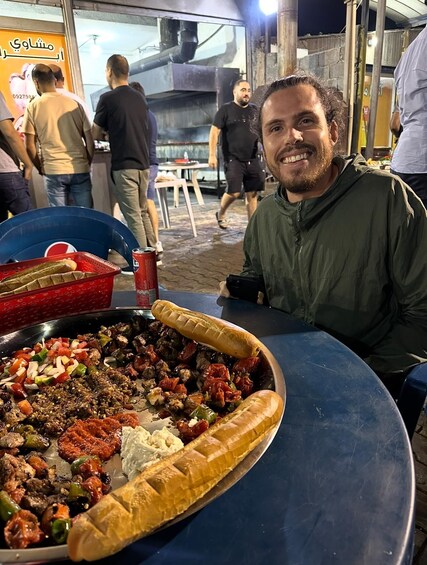 A person sitting at a table with a large platter of food, including meats, vegetables, and bread. 1