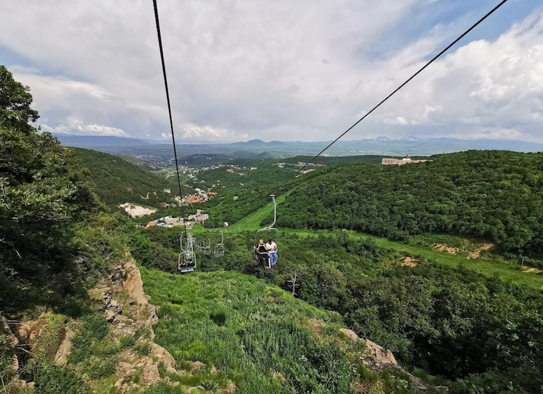 A cable car system in a mountainous area with lush greenery and distant buildings. 2