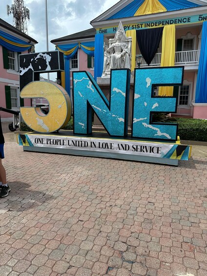 A large sign with the word "ONE" and the phrase "ONE PEOPLE UNITED IN LOVE AND SERVICE" in front of a building with colorful drapes and a statue. 5