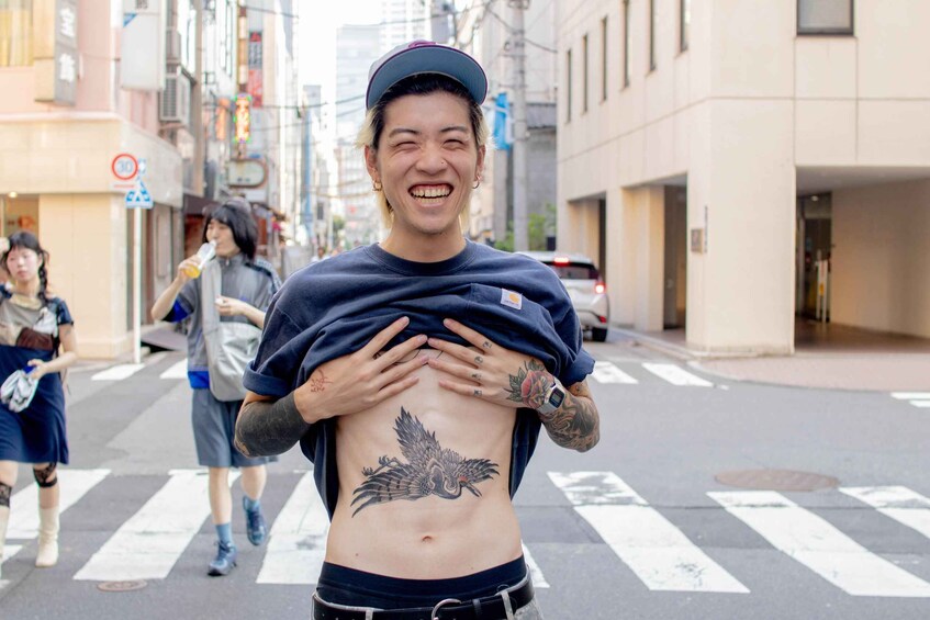 A person with a tattoo on their abdomen standing on a crosswalk in an urban street. 1