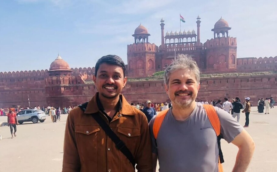 Two men standing in front of a large historic fort with multiple domes and towers. 2