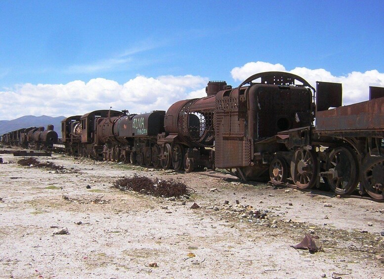 A row of rusted, abandoned trains in a desert landscape with mountains in the background. 2