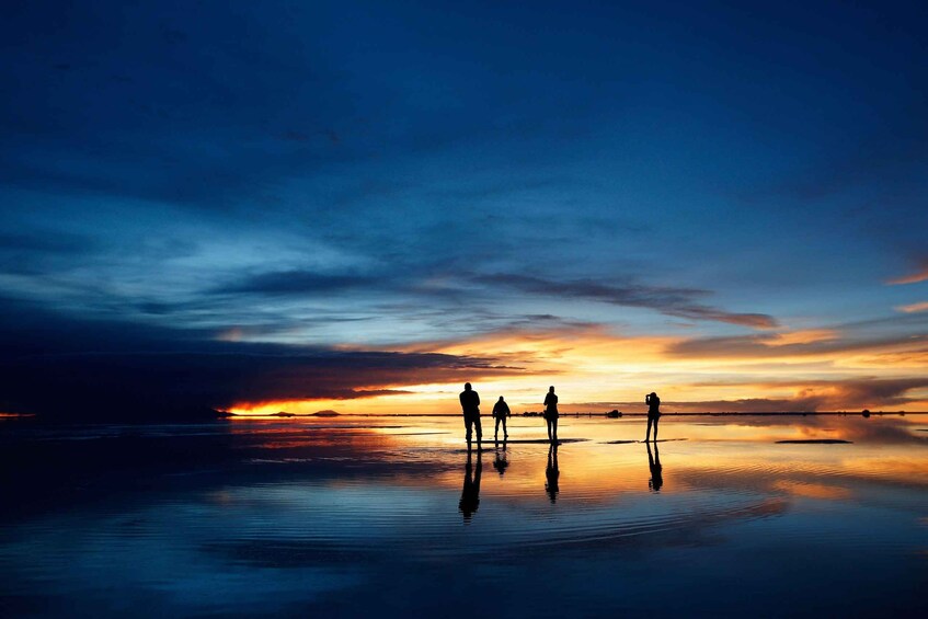 A sunset over a calm body of water with silhouettes of people standing on the shore. 3