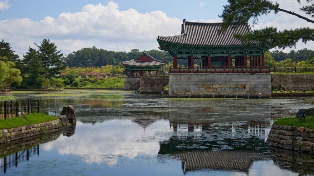 A traditional Korean pavilion by a calm pond, surrounded by lush greenery and a clear sky. 2