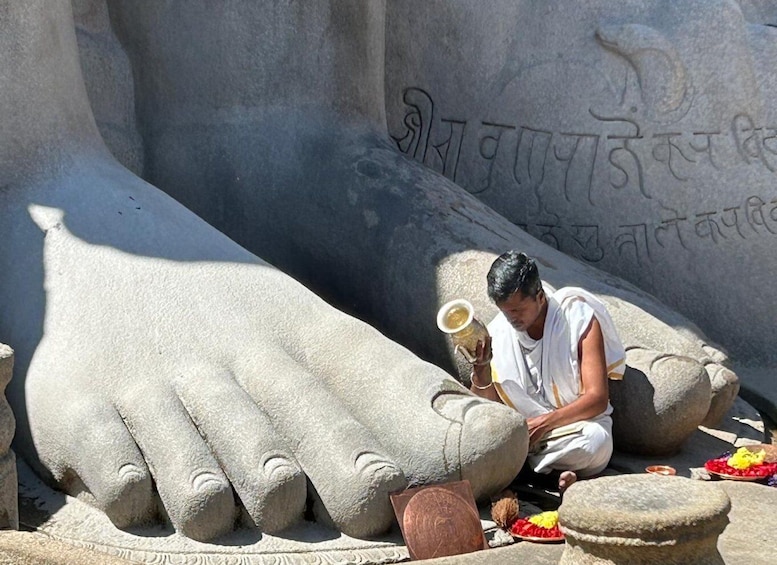 A man performing a ritual with a large stone hand sculpture, surrounded by offerings. 1