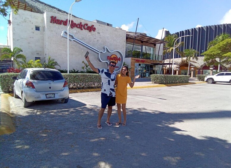 A Hard Rock Cafe with a large guitar sign, a parking lot, and a building with a modern design in the background. 1