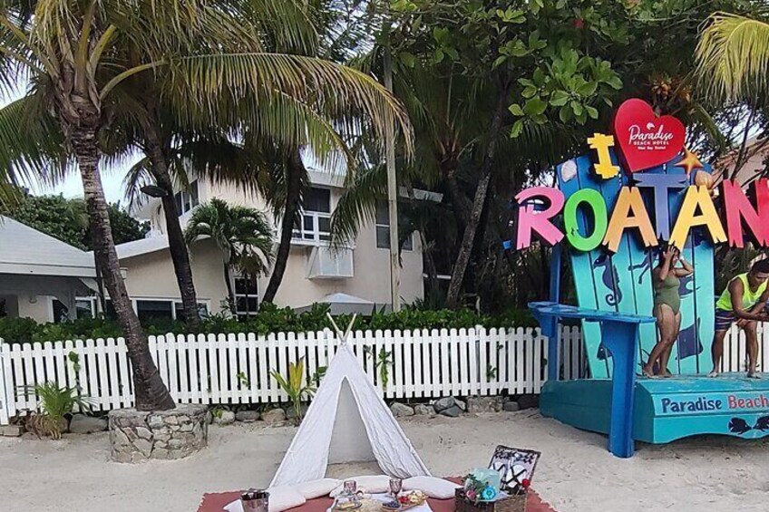 Una playa con una tienda de campaña, un cartel que dice "Paradise Beach" y palmeras. 1