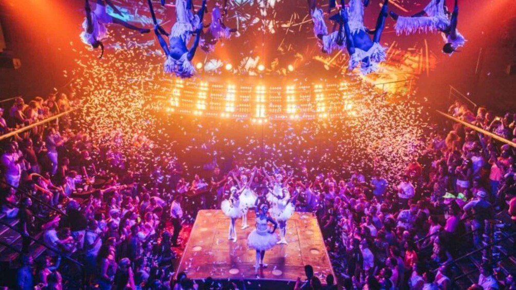 A crowded concert with a stage at the center, illuminated by stage lights. 3