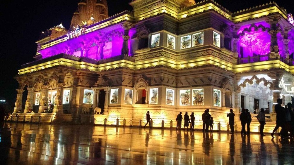 A brightly lit temple with intricate carvings and statues, illuminated by purple and yellow lights. 3